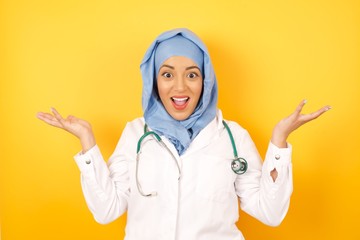 young beautiful Arab doctor woman wearing medical uniform standing over yellow background, celebrating crazy and amazed for success with arms raised and open eyes screaming excited. Winner concept