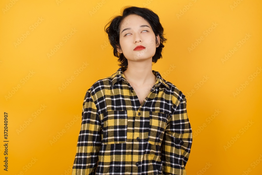 Young asian woman with short hair wearing plaid shirt standing over yellow background looking sleepy and tired, exhausted for fatigue and hangover, lazy eyes in the morning. - obrazy, fototapety, plakaty 