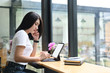 © Prathankarnpap - A beautiful woman is using a computer tablet with a white blank screen while sitting at the wooden counter bar.