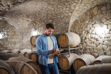 Man worker with clipboard indoors, wine making concept.