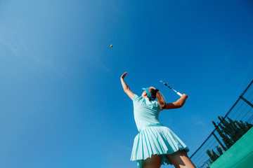 low angle shot of a teenage girl playing tennis, throwing ball up and serving