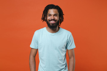 Wall Mural - Smiling cheerful young african american man guy wearing blue casual t-shirt posing isolated on bright orange wall background studio portrait. People sincere emotions lifestyle concept. Looking camera.