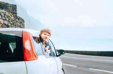 Wall Mural - Blonde hair teenager boy looking out from the rear passangers door of economy class auto and smiling.Rental car and Traveling by auto concept image.