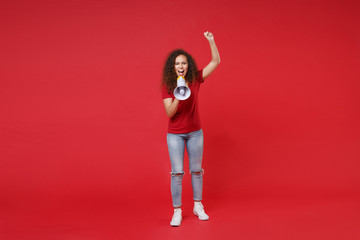 Wall Mural - Full length portrait of young african american girl in casual t-shirt isolated on red background studio portrait. People lifestyle concept. Mock up copy space. Screaming in megaphone clenching fist.