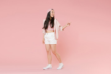Wall Mural - Full length portrait of smiling young asian girl in casual clothes, cap isolated on pastel pink background studio portrait. People lifestyle concept. Mock up copy space. Pointing index finger aside.