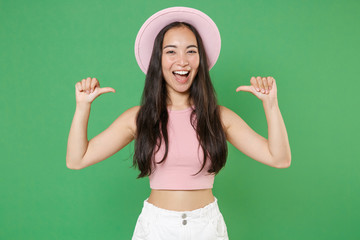 Cheerful young asian woman girl in casual pink clothes hat isolated on green wall background studio portrait. People sincere emotions lifestyle concept. Mock up copy space. Pointing thumbs on herself.