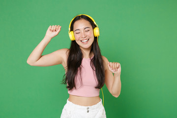 Wall Mural - Smiling young asian woman girl in casual pink clothes isolated on green wall background studio portrait. People emotions lifestyle concept. Mock up copy space. Listening music with headphones dancing.