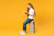 © ViDi Studio - Full length young redhead girl 12-13 years old in white t-shirt jeans sit on big stack school textbook notebook read book isolated on yellow background children studio portrait Kids education concept