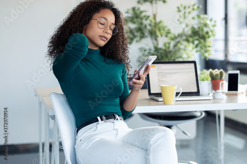 Fotomural Tired young woman with neck pain holding her mobile phone at the office