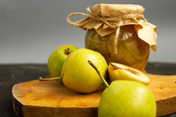 Pear jam in a glass jar. The jar is covered with craft paper and tied with a jute rope. Sweet jam stands on a cutting board and fresh yellow pear fruits lie nearby