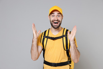 Wall Mural - Delivery employee man guy male 20s in yellow cap t-shirt uniform thermal food bag backpack work courier service during quarantine coronavirus covid-19 virus, posing isolated on gray background studio.