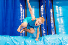 Child On Blue Playground Trampoline. Kids Jump In Inflatable Bounce Castle On Kindergarten Birthday Party. Activity And Play Center For Young Child.