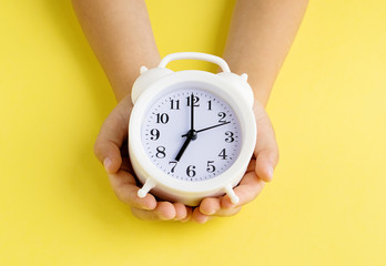 Children's hands hold a white alarm clock . Yellow background. Concept of time. Copy spase