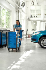 African american woman, professional female mechanic in uniform pulling, carrying tool box cart in auto repair shop. Car service, maintenance and people concept