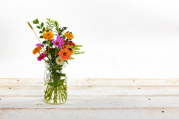 Colorful summer wildflowers in a clear jar on an old wooden table isolated on white with a shallow depth of field