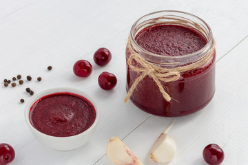 Spicy red cherry sauce for meat or fish on a white wooden background. Copy space