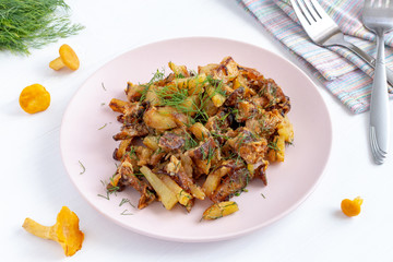 Fried forest chanterelle mushrooms with potatoes on a plate. Vegan and vegetarian dish on white wooden background