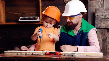 Wall Mural - Father and son in protective helmets twist the screw. Dad is proud of his boy who twists the screw. Fathers supports.