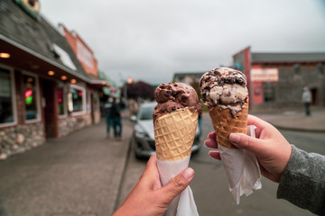 Two people hands hold ice cream waffle cones in a toasting gesture, while walking around. Taken in downtown Seaside, Oregon