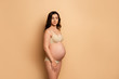  pregnant woman in lingerie looking away while standing on beige