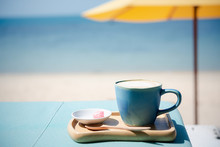 Summer Blue Coffee Latte Cup By The Beach  With Yellow Umbrella Background