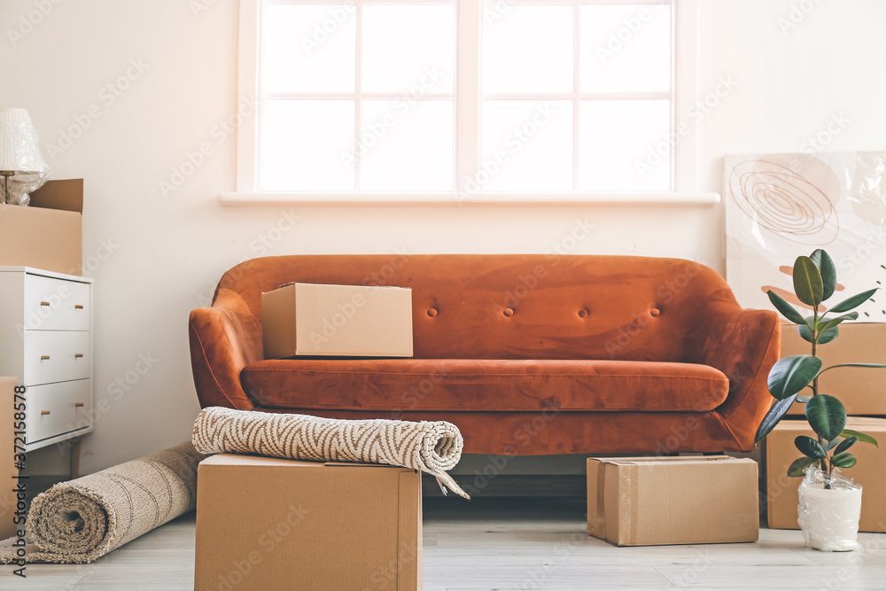 Cardboard boxes with belongings and sofa in new flat on moving day