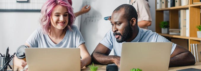 Panoramic shot of businesswoman using laptop near american colleague in office