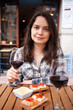 Portrait of smiling young woman spending time on open terrace of restaurant with wine and snacks