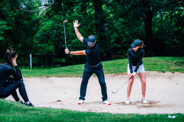 Golf sand practice shots. Young woman having a lesson with golf instructor