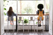 Two diverse young women sitting apart at cafe table, African and Caucasian girls working or studying, dining in cafeteria avoiding communication, social distancing safety indoors concept, back view.
