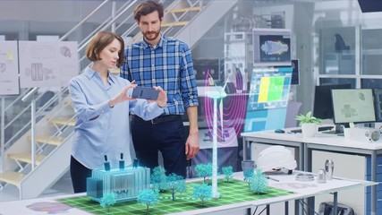 Wall Mural - green energy concept: two ecological engineers use augmented reality smartphone to design 3d wind tu