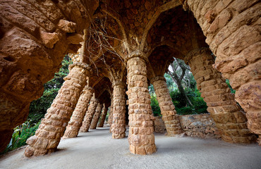 Barcelona, Spain. Park Guell. Antonio Gaudi Art Architecture. Stone pillars with archs at sunset among green trees and plants. Famous touristic destination landmark for walking tours.