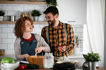 Wall Mural - Young couple making delicious food at home. Loving couple enjoying in the kitchen..