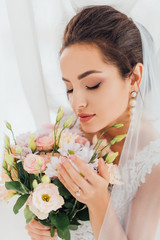 Wall Mural - Selective focus of young bride in wedding dress and veil touching flowers beside curtains