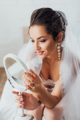 Wall Mural - Selective focus of bride in bra and veil looking at mirror in bedroom