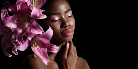 Wall Mural - beauty portrait of young african american model with pink art make up posing with lily flowers isola