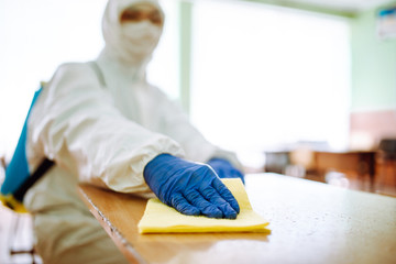 Wall Mural - Closeup of a man from disinfection group cleans up the desk at school with a yellow rag. Professional worker sterilizes the classroom to prevent covid-19 spread. Healthcare of pupils and students.