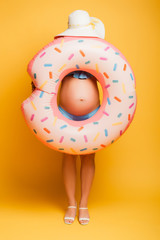 Wall Mural - pregnant woman in straw hat hiding behind swim ring on yellow