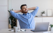 © Prostock-studio - Smiling millennial businessman leaning back in chair at workplace, resting in office