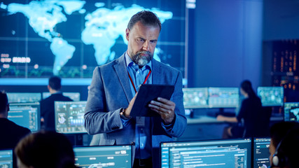 Aufkleber - Male Project Leader is Standing with Tablet Computer and Checking Work Data. Science Engineers Work Around Him. Telecommunications Control Monitoring Room with a Global Map on Big Screen.