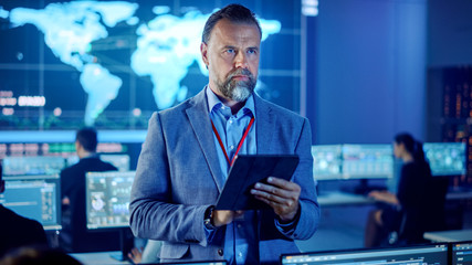Aufkleber - Male Project Leader is Standing with Tablet Computer and Making Mental Calculations. Data Science Engineers Work Around Him. Telecommunications Control Monitoring Room with a Global Map on Big Screen.