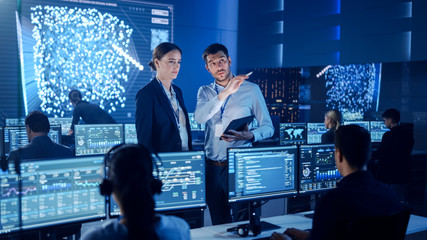 Project Manager and Computer Science Engineer Talking while Using A Digital Tablet Computer. Telecommunications Company System Control and Monitoring Office Room with Working Specialists.