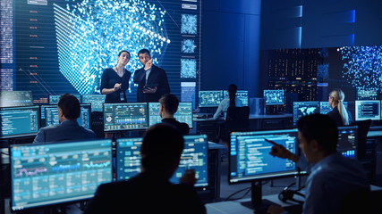 Project Manager and Computer Science Engineer Talking while Using A Digital Tablet Computer. Telecommunications System Control Monitoring Room with Neural Network on Big Screen.