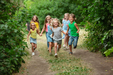 Wall Mural - Happiness. Kids, children running on green forest. Cheerful and happy boys and girs playing, laughting, running through green blooming meadow. Childhood and summertime, sincere emotions concept.