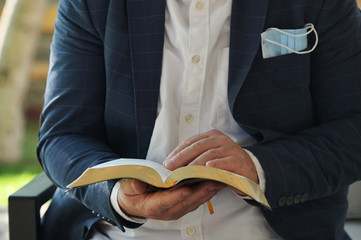 Man Reading Holy Bible with a medical mask sticks out of a pocket