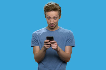 Surprised teenage boy using mobile phone. Trendy teen guy using app on his smartphone against color background.