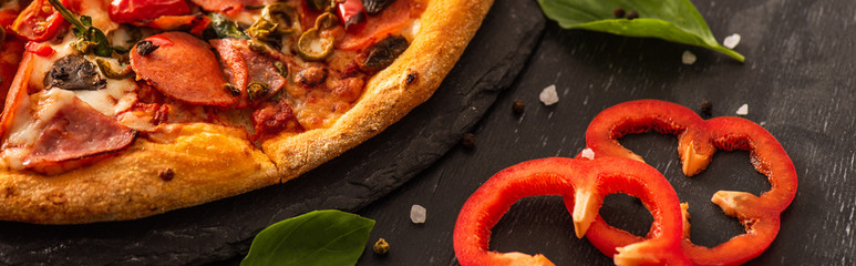 Wall Mural - close up view of delicious Italian pizza with salami near vegetables on black background, panoramic shot