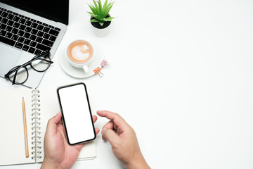 Wall Mural - Flat lay, workspace business office concept on white table desk with hand holding blank screen phone and laptop computer, coffee cup and glasses, blank notepad and pencil, top view with copy space