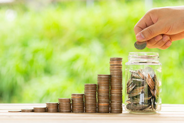 White hand man holding coin to putting in Jar or glass bottle for saving with green background. Saving money, Saving concept