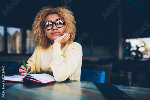 Fotografía Thoughtful young woman in eyeglasses writing to do list of goals writing in diar
